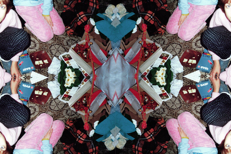 Ein mittig gespiegeltes Foto, das von oben auf eine Szene blickt: Man sieht an den Bildrändern die Beine von Kindern, die auf einem Teppich um verschiedene Gegenstände herum sitzen.