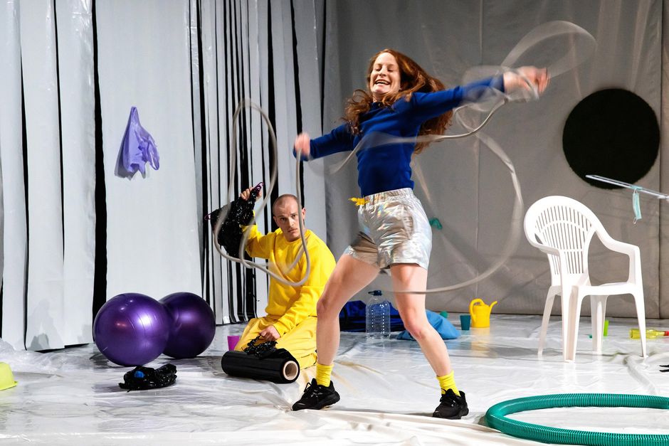 Jan Rozman, Julia Keren Turbahn | Dinge Dingen Zwei Personen auf einer Bühne, die eine trägt gelbe Klamotten und kniet auf dem Boden, die ist aufrecht in einer Bewegung und hält ein Seil in den Händen. Um sie herum befinden sich verscheidene Dinge.